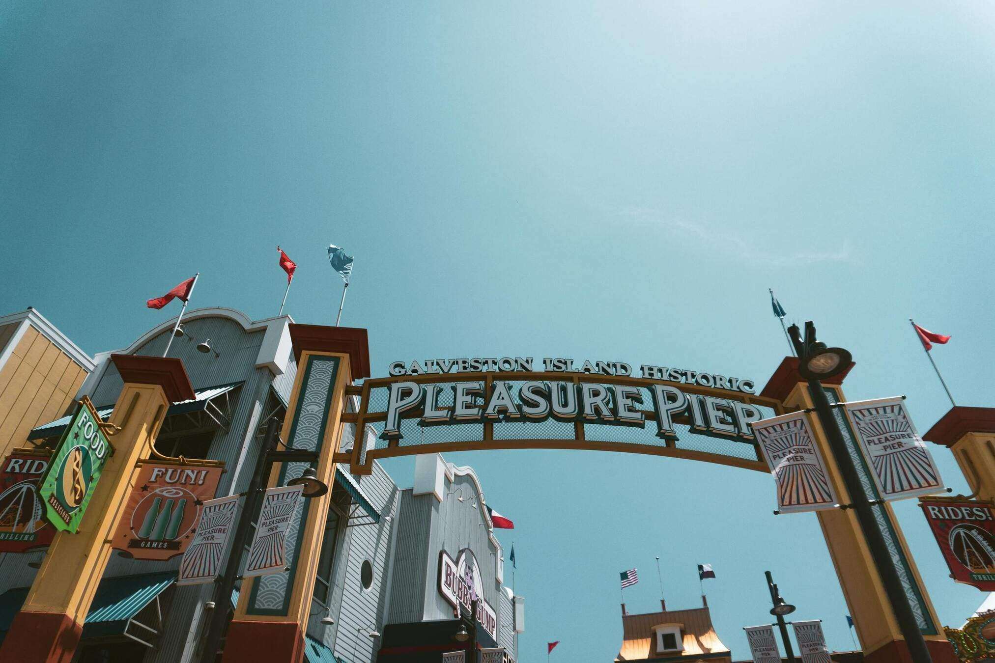 View of the iconic Galveston Island Historic Pleasure Pier entrance under a bright blue sky.