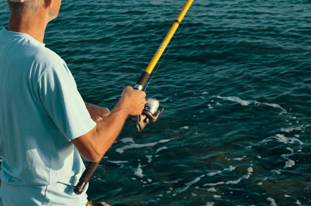 Person fishing with a rod along the Gulf of Mexico shoreline, standing near the water’s edge on a calm day.