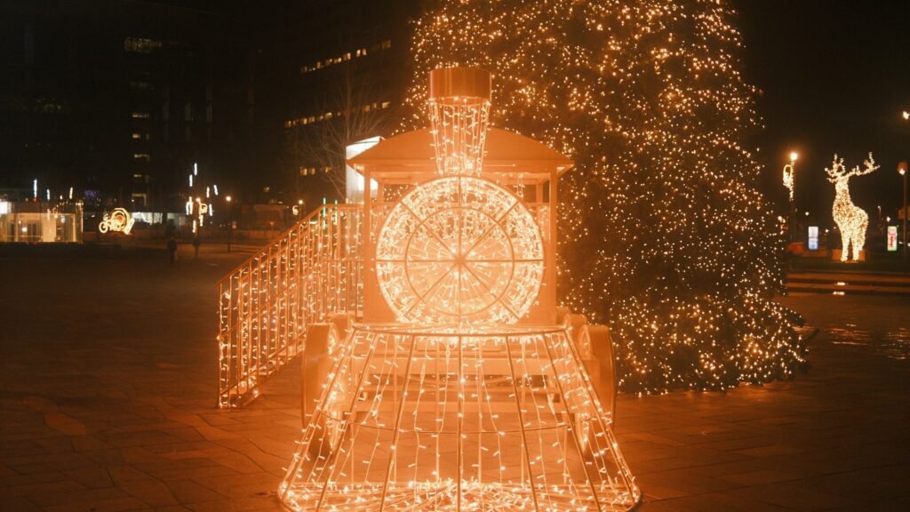 Train made of Christmas lights next to a lit tree at night