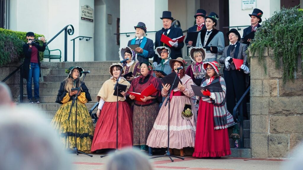 Carolers in Victorian costumes singing Christmas songs